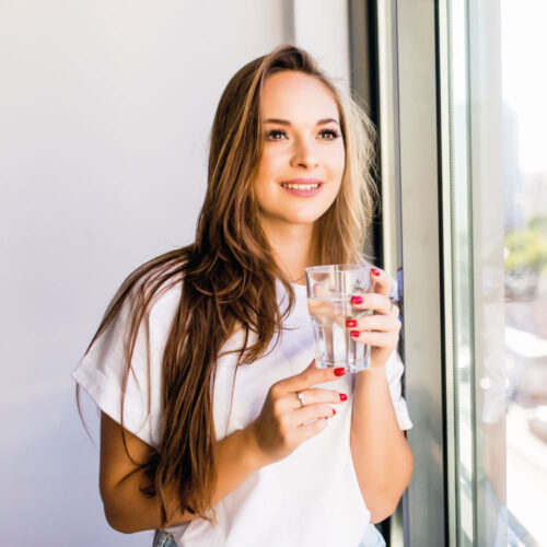 Young woman with glass of water next to window | Aesthetics Beauty Boutique | Miami Florida